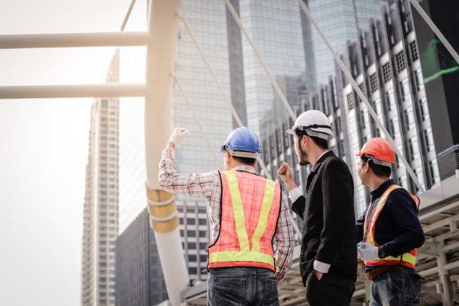 Contractors assess construction progress at a commercial building site in a city skyline during daylight