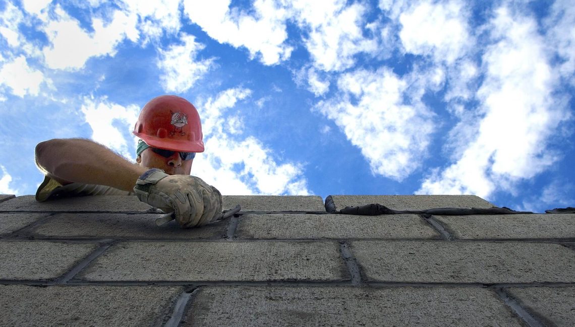 Commercial building renovation specialists working on masonry wall under clear blue sky