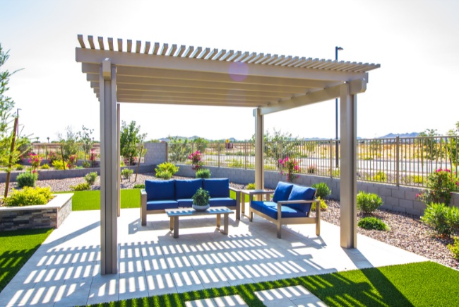 Concrete patio construction highlighted by a shaded seating area equipped with blue cushions in a landscaped outdoor space