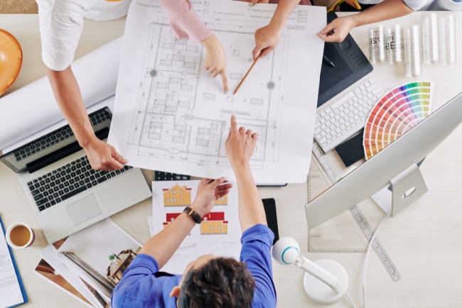 Collaboration among design build contractors while reviewing architectural plans on a workspace table