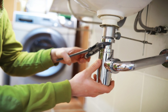 Emergency plumbing service fixing a sink trap in a residential kitchen during the day