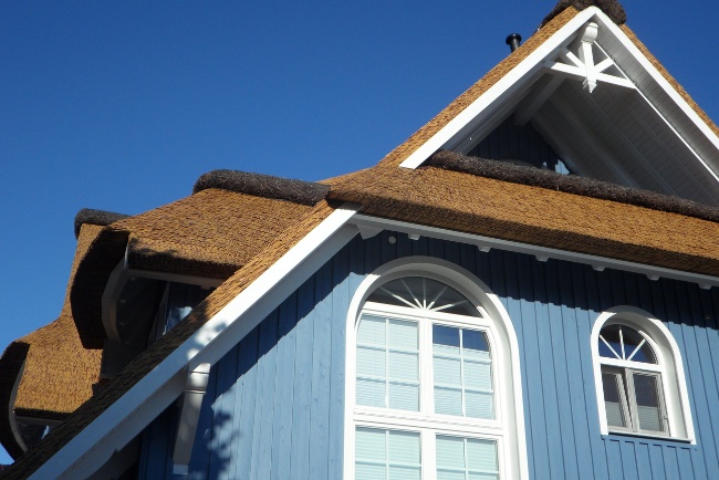 Flat roof repair project on a well-maintained residential building with a thatched roof and blue siding