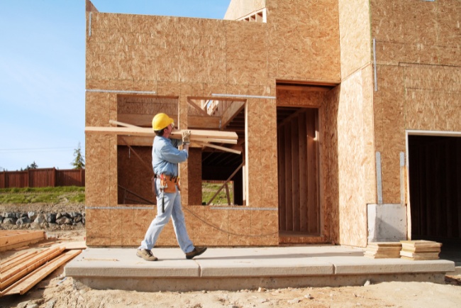 Luxury new construction home with worker carrying building materials on a clear day