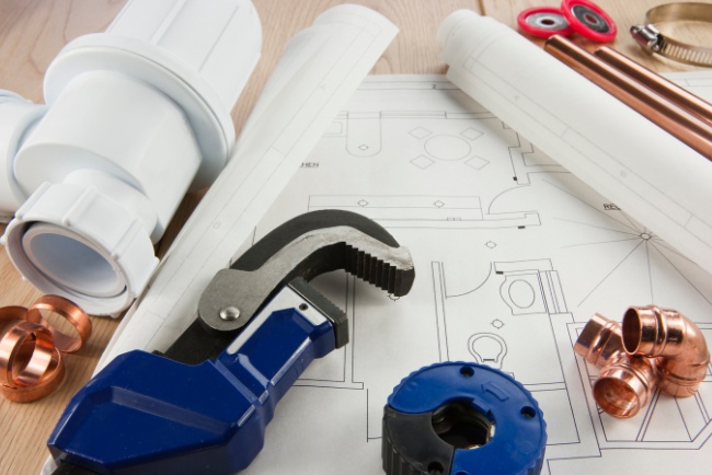 Plumbing maintenance tools and plans laid out on a wooden surface in a service area