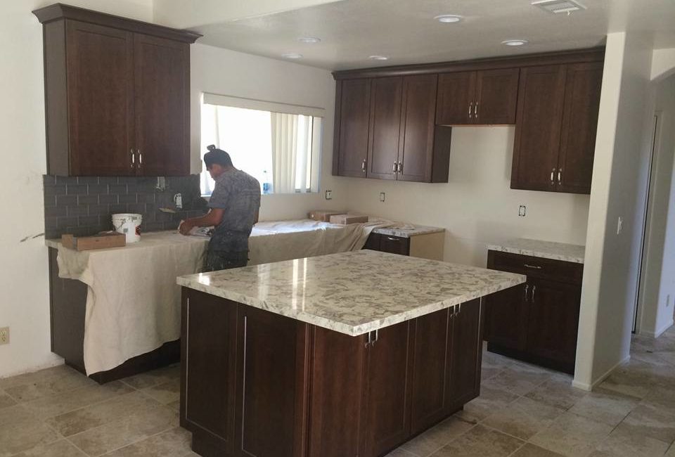 Residential construction specialists installing cabinets and countertops in a modern kitchen during daylight