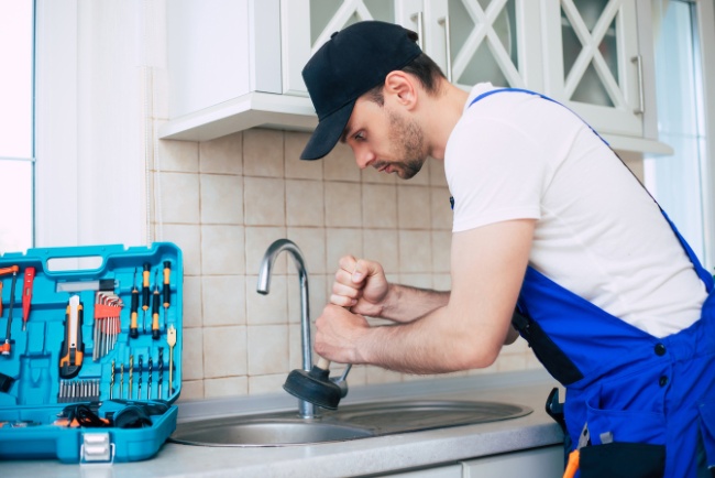 Professional plumber repairing kitchen sink with tools during residential plumbing service